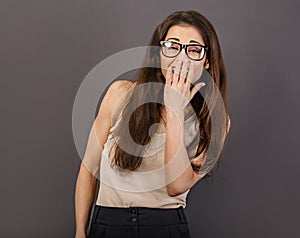 Beautiful toothy laughing smiling business woman in glasses covering the mouth the hand in white shirt on grey background with