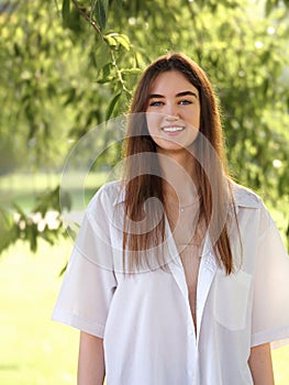 Beautiful toothy smiling teen woman looking happy outdoors summer green trees background. Closeup portrait in bright sunny day