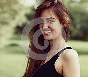 Beautiful toothy smiling teen woman looking happy outdoors on summer green trees background. Closeup portrait in bright sunny day