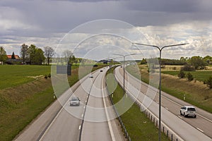 Beautiful top view of E4 highway with several cars. Green side fields and stormy sky background.