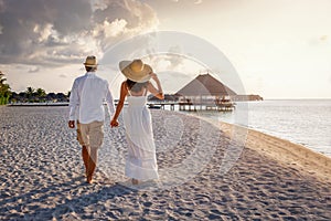 A beautiful tourist couple in white summer clothing walks along a tropical beach