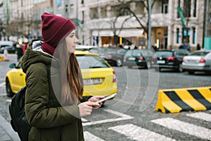 Beautiful tourist girl with a tablet on a street in Prague calls a taxi or looks at a map or uses the Internet or a