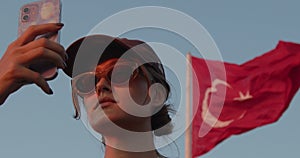 A beautiful tourist girl takes a view of the city on her phone against the background of the waving flag of Turkey in