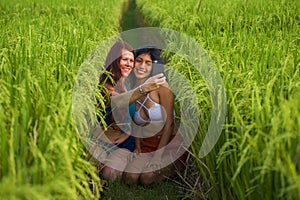 Beautiful tourist girls taking girlfriends selfie together with mobile phone in rice field nature landscape smiling enjoying