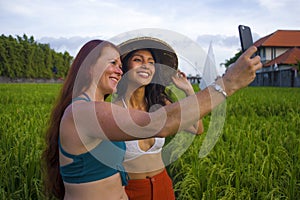 Beautiful tourist girls taking girlfriends selfie together with mobile phone in rice field nature landscape smiling enjoying