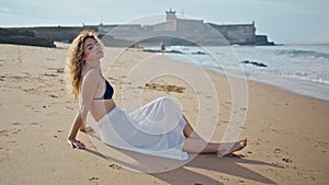 Beautiful tourist sitting beach sunny day looking camera. Woman relaxing at sand