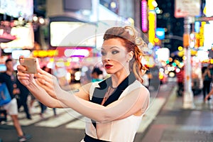 Beautiful tourist woman fashion blogger taking photo selfie on night Time Square in New York City