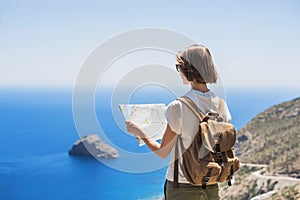 Beautiful tourist woman holding map, traveler girl looking for hiking route with sea and mountain at background.