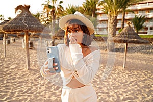 Beautiful tourist woman talking with friends on videochat using mobile phone. Summer beach vacation. Happy lifestyle