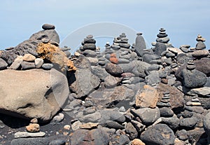 Beautiful towers of stacked pebbles and stones in a large arrangement on a black sand beach with blue sky