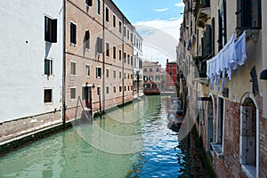 Beautiful, tranquil view in Venice, Italy, with boats parked on canal surrounded by picturesque old buildings under blue sky