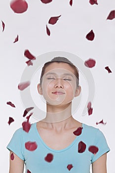 Beautiful tranquil young woman looking up with eyes closed with rose petals flying around her