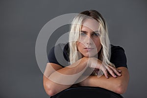 Beautiful transgender woman leaning on chair over gray background