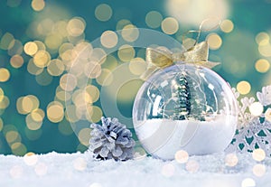 Beautiful transparent Christmas ornament with small fir tree on snow against blurred lights, bokeh effect. Space for text