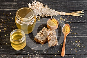 Beautiful transparent honey in bank, honeycombs and pollen on a wooden table