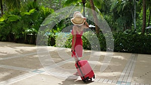 Beautiful traveler woman girl in red dress walking with suitcase at luxury resort