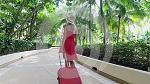 Beautiful traveler woman girl in red dress walking with suitcase at luxury resort
