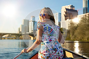 A beautiful traveller enjoying a tourist attraction adventure, kayaking the river near an urban city skyline in the summer