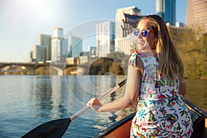 A beautiful traveller enjoying a tourist attraction adventure, kayaking the river near an urban city skyline in the summer