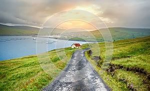 Beautiful trekking path at sunset with green meadows and views of the bay and Village of Sandavagur, Faroe Islands, Denmark, in