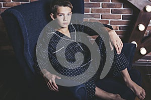 Beautiful trendy teen boy sitting on a chair at home