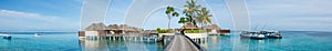 Beautiful tropical beach panorama of bungalos with bridge near the ocean with palms trees and boats at Maldives