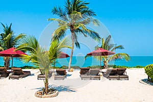 Beautiful tropical beach sea ocean with umbrella and chair around coconut palm tree on blue sky