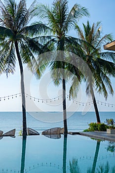 Beautiful tropical beach and sea with palm tree, coconut tree and chair around swimming pool in hotel resort for travel and