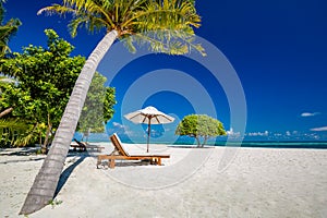 Beautiful tropical island scenery, two sun beds, loungers, umbrella under palm tree. White sand, sea view with horizon