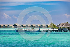 Beautiful tropical Maldives beach under cloudy sky with dhoni boat and water villas, bungalows. Luxury vacation