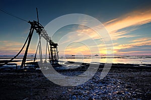 Beautiful tropical sunset background, wooden water pump tower on the muddy beach. cloudy and yellow sky