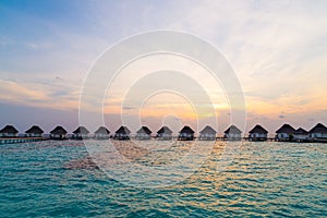 Beautiful tropical sunset over Maldives island with water bungalow in hotel resort