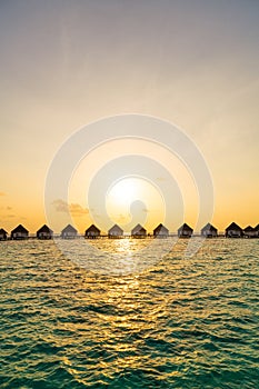 Beautiful tropical sunset over Maldives island with water bungalow in hotel resort