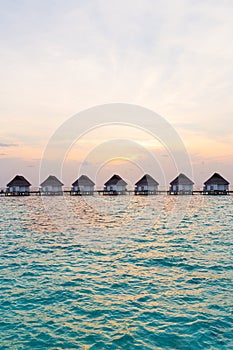 Beautiful tropical sunset over Maldives island with water bungalow in hotel resort