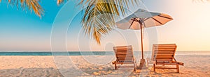 Beautiful tropical sunset scenery, two sun beds, loungers, umbrella under palm tree. White sand, sea view with horizon, colorful