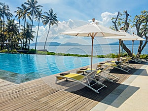 Beautiful tropical swimming pool in hotel or resort with umbrella, coconuts tree sun-loungers, palm trees with infinity pool view