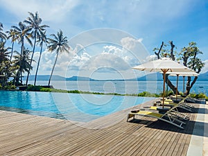 Beautiful tropical swimming pool in hotel or resort with umbrella, coconuts tree sun-loungers, palm trees with infinity pool view