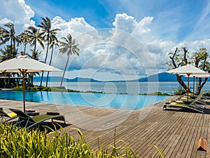 Beautiful tropical swimming pool in hotel or resort with umbrella, coconuts tree sun-loungers, palm trees with infinity pool view