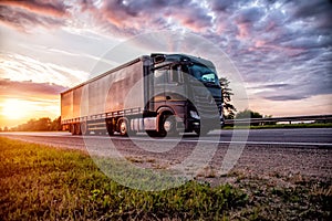 A beautiful truck tractor with a semitrailer transports cargo against the backdrop of a sunset in the evening and a