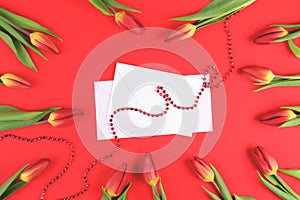 Beautiful tulips around white envelope and blank card on red background