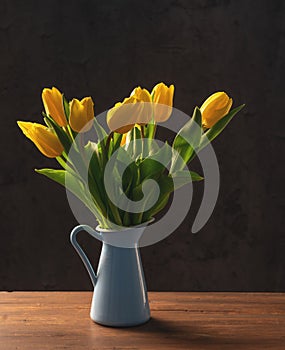 beautiful tulips in a blue vase on a dark wooden table on a dark background