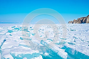 Beautiful turquoise blue ice on the Frozen Lake Baikal with mountains on the background.