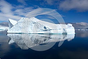 Beautiful turquoise iceberg with texture and cave on beautiful day in Antarctica reflecting in calm water