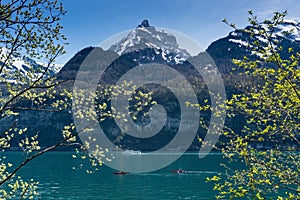 Beautiful turquoise mountain lake panorama with snow-covered peaks and green meadows and forests and boats on the lake