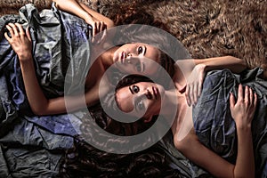 Beautiful twins young women with natural make-up and hair style lying with their curly hair surround them
