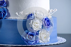 Beautiful two tiered white and blue wedding cake decorated with flowers sugar roses. Concept of elegant holiday desserts