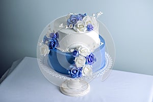 Beautiful two tiered white and blue wedding cake decorated with flowers sugar roses. Concept of elegant holiday desserts