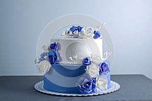 Beautiful two tiered white and blue wedding cake decorated with flowers sugar roses. Concept of elegant holiday desserts