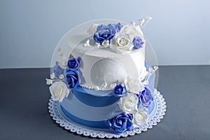 Beautiful two tiered white and blue wedding cake decorated with flowers sugar roses. Concept of elegant holiday desserts