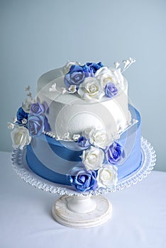 Beautiful two tiered white and blue wedding cake decorated with flowers sugar roses. Concept of elegant holiday desserts